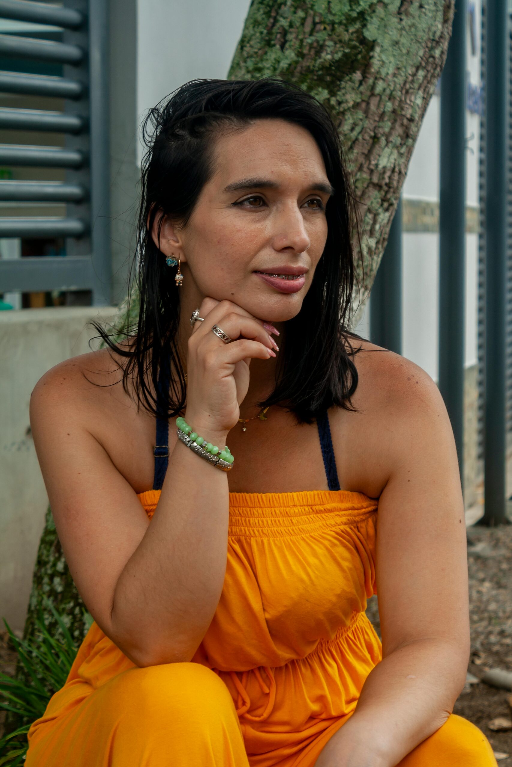 A thoughtful woman in a yellow dress sits outdoors, offering a serene summer portrait.